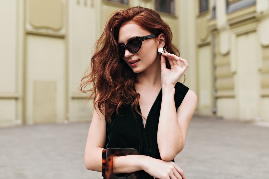 Curly woman in sunglasses touching her massive earrings