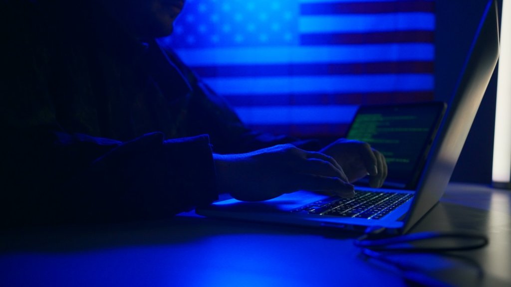 Hacker with laptop and USA flag in background. Cyber attack concept