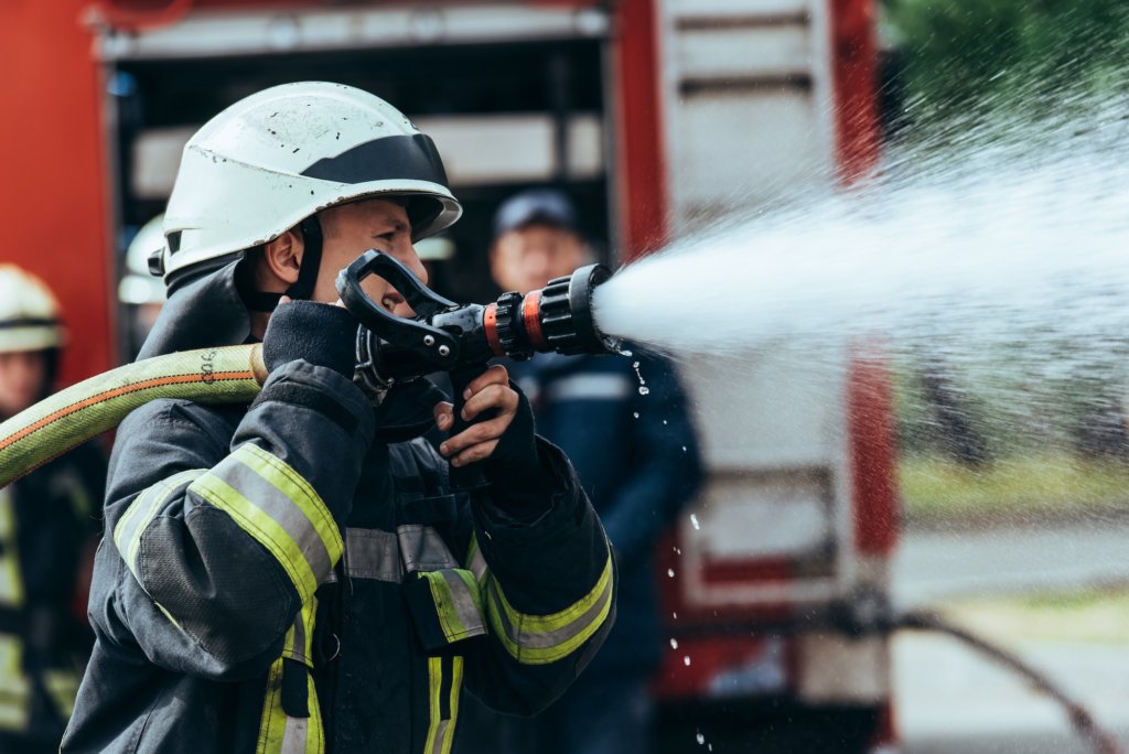 selective focus of firefighter with water hose extinguishing fire on street