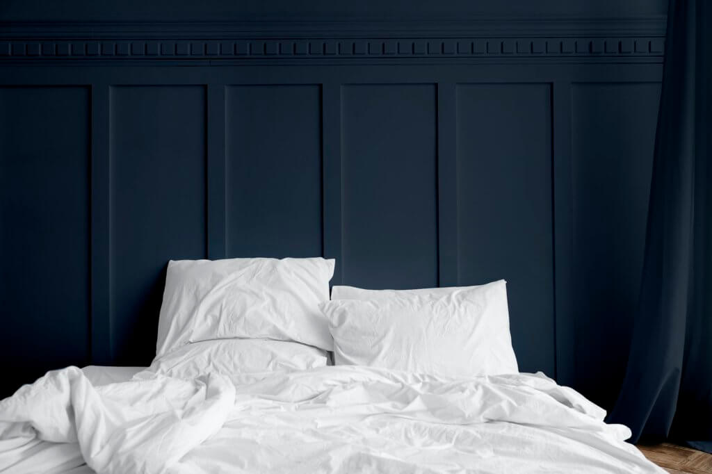 White bed linen on a mattress in a midnight blue bedroom
